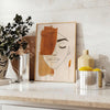 Poster showing abstract line art in green and orange, minimalist composition - styled on a counter with eucalyptus and a bowl of lemons