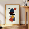 Minimalist Scandinavian abstract poster with orange and white geometric shapes - beside a round wooden side table with books