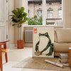 A green and orange frog with an angry expression in a retro space style - in a Parisian living room with a sofa and a fig plant