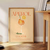 Poster showing stylized Aperol cocktail illustration in orange and gray tones - beside a round wooden side table with books