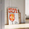 Poster raffigurante un Aperol Spritz stilizzato in arancione e nero - appoggiato su un pavimento a spina di pesce contro una parete a pannelli