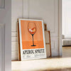 Minimalist graphic art of an Aperol Spritz cocktail in orange and black - leaning on a herringbone floor against a white panelled wall