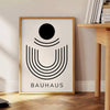 Poster Bauhaus geometrico grigio e nero con forme astratte minimaliste - accanto a un tavolino rotondo in legno con libri