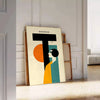 Poster mit minimalistischer geometrischer Menschendarstellung im klassischen Bauhaus-Stil - an eine weiße Paneelwand gelehnt auf Fischgrätparkett