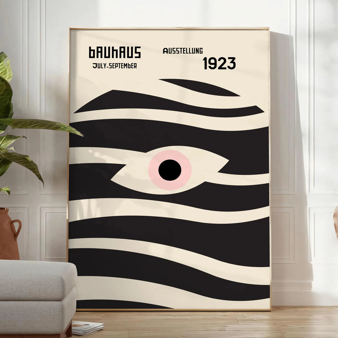 Poster showing geometric abstract Bauhaus composition with bold shapes - in a bright minimalist room with a plant and an armchair