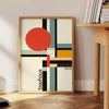 Bauhaus-Poster mit geometrischem Design in Orange und Schwarz - neben einem runden Beistelltisch aus Holz mit Büchern