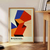Cartel Bauhaus con diseño geométrico abstracto en rojo y naranja - junto a una mesa auxiliar redonda de madera con libros