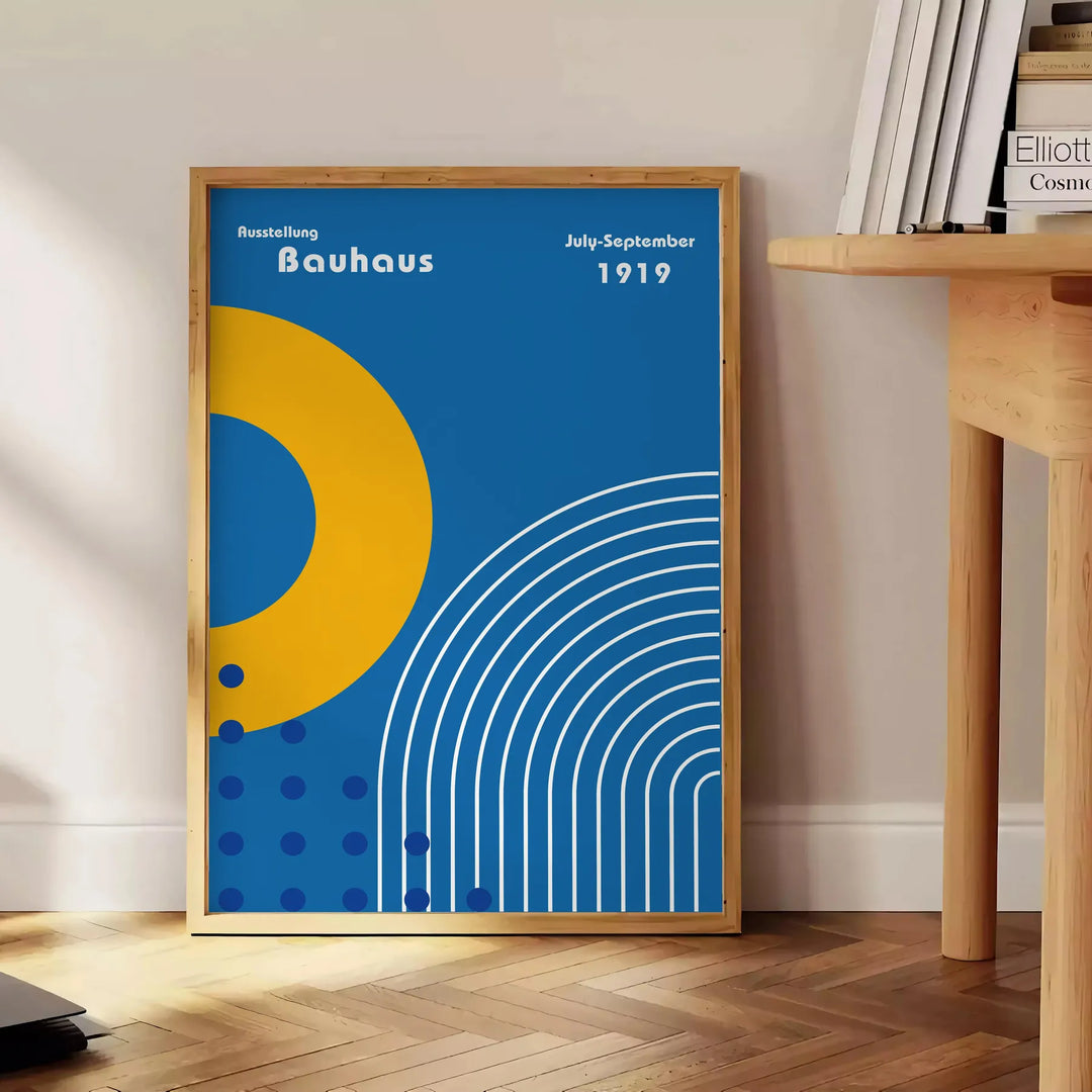 Minimalistyczny plakat Bauhaus z szarymi i żółtymi kształtami geometrycznymi - obok okrągłego drewnianego stolika z książkami