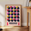 Schwarz-gelbes Bauhaus Plakat mit geometrischem abstraktem Design und kräftigen Formen - neben einem runden Beistelltisch aus Holz mit Büchern