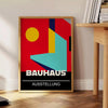 Bauhaus geometric poster in bold red and yellow abstract shapes - beside a round wooden side table with books