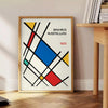 White and red geometric Bauhaus poster with bold minimalist abstract composition - beside a round wooden side table with books