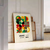 Poster Bauhaus con composizione geometrica astratta in verde e rosso intensi - appoggiato su un pavimento a spina di pesce contro una parete a pannelli