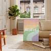 Abstract design with the word 'Believe' in green and orange hues - in a Parisian living room with a sofa and a fig plant