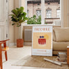 Abstract illustration of a bramble cocktail with orange and blue splashes - in a Parisian living room with a sofa and a fig plant