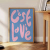 Abstract design with brown and green tones featuring the phrase 'C'est La Vie' - beside a round wooden side table with books