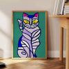 A modern art depiction of a cat in abstract shapes with green and blue tones - beside a round wooden side table with books