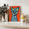 A modern art print featuring a stylized cat in blue and brown tones - styled on a counter with eucalyptus and a bowl of lemons
