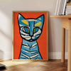 A modern art print featuring a stylized cat in blue and brown tones - beside a round wooden side table with books