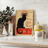 A vintage poster featuring a black cat with a yellow background, text reading 'Chat Noir'. - styled on a counter with eucalyptus and a bowl of lemons