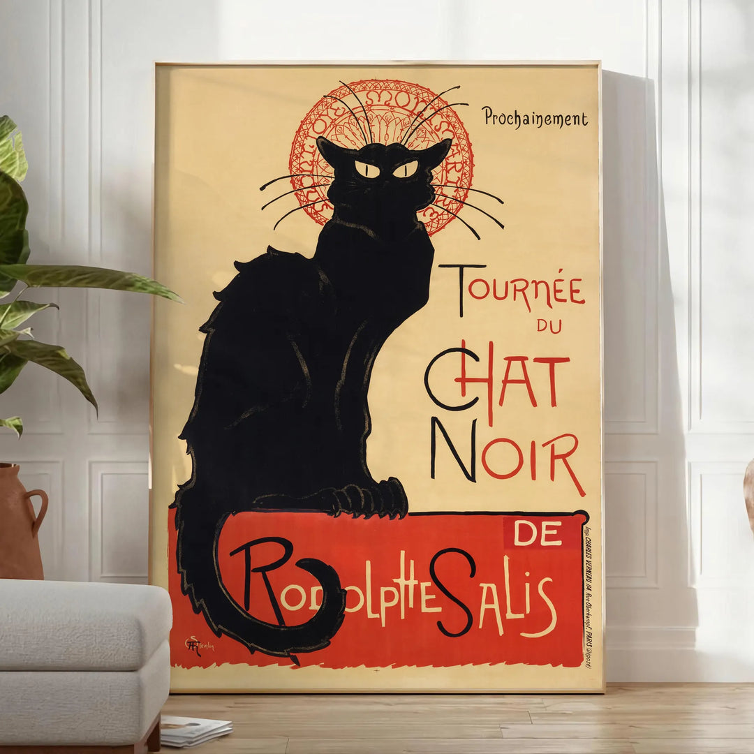 A vintage poster featuring a black cat with a yellow background, text reading 'Chat Noir'. - in a bright minimalist room with a plant and an armchair