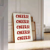 シンプルなデザインで「Cheers」の文字がグレーとホワイトで表現されています - ヘリンボーンの床に立てかけ、白いパネル壁を背景に