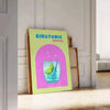 A gin and tonic cocktail in a glass with green and blue hues - leaning on a herringbone floor against a white panelled wall