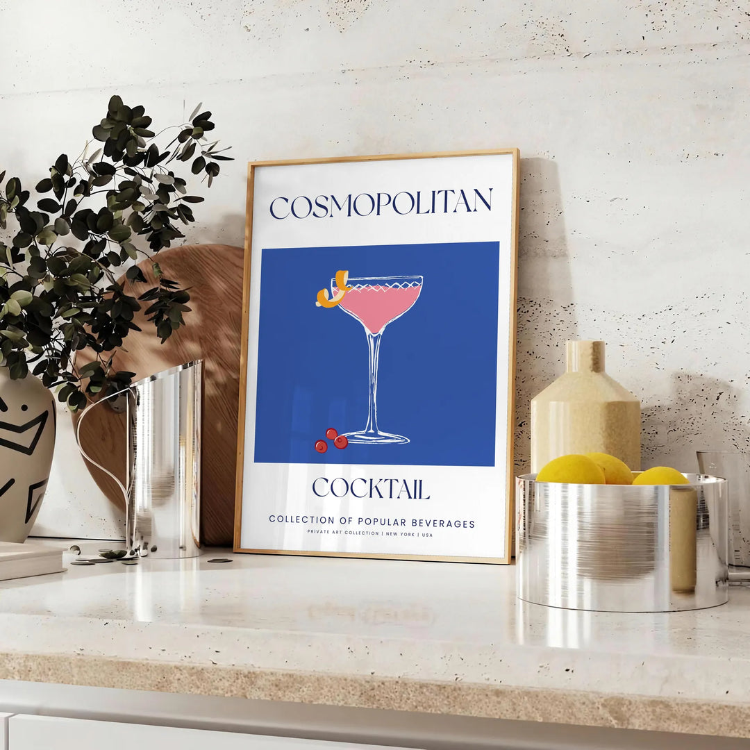 A stylish illustration of a cosmopolitan cocktail against a blue backdrop - styled on a counter with eucalyptus and a bowl of lemons