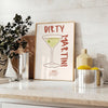 Illustration of a dirty martini cocktail in a glass, with olive garnish - styled on a counter with eucalyptus and a bowl of lemons