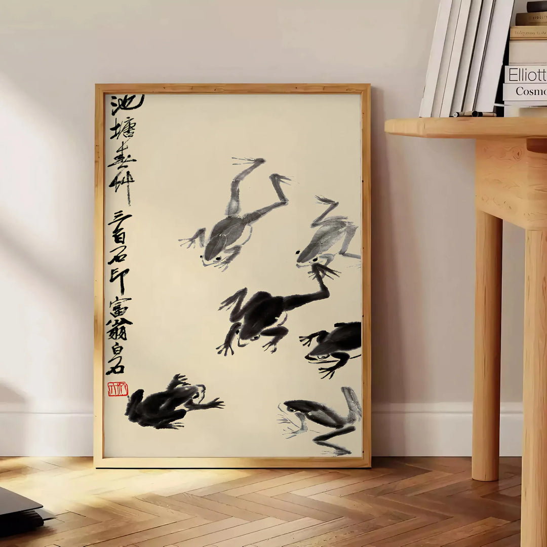 A stylized frog illustration in black and orange, inspired by Matsumoto Hoji, Japan - beside a round wooden side table with books