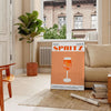 A sleek black background with a vibrant orange cocktail spritz illustration - in a Parisian living room with a sofa and a fig plant