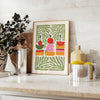 A colorful kitchen print featuring shades of green and orange - styled on a counter with eucalyptus and a bowl of lemons