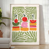 A colorful kitchen print featuring shades of green and orange - in a bright minimalist room with a plant and an armchair