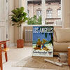 Vintage travel poster featuring Los Angeles with green palm trees and white lettering - in a Parisian living room with a sofa and a fig plant
