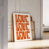 Un poster motivant avec la phrase 'Love Love Love' dans des tons chauds de marron et d'orange - posée sur un parquet à chevrons contre un mur à moulures