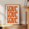 Un poster motivant avec la phrase 'Love Love Love' dans des tons chauds de marron et d'orange - à côté d'une table d'appoint ronde en bois avec des livres