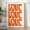 Un poster motivant avec la phrase 'Love Love Love' dans des tons chauds de marron et d'orange - dans une pièce lumineuse épurée avec plante et fauteuil