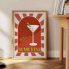 A colorful illustration of a martini cocktail with green and orange accents - beside a round wooden side table with books