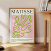 Abstrakcyjne kształty w zieleni i różu, inspirowane stylem Matisse'a - obok okrągłego drewnianego stolika z książkami