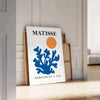 Matisse cut-paper style poster showing abstract black and orange shapes - leaning on a herringbone floor against a white panelled wall