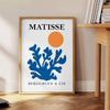 Matisse cut-paper style poster showing abstract black and orange shapes - beside a round wooden side table with books