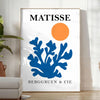 Matisse cut-paper style poster showing abstract black and orange shapes - in a bright minimalist room with a plant and an armchair
