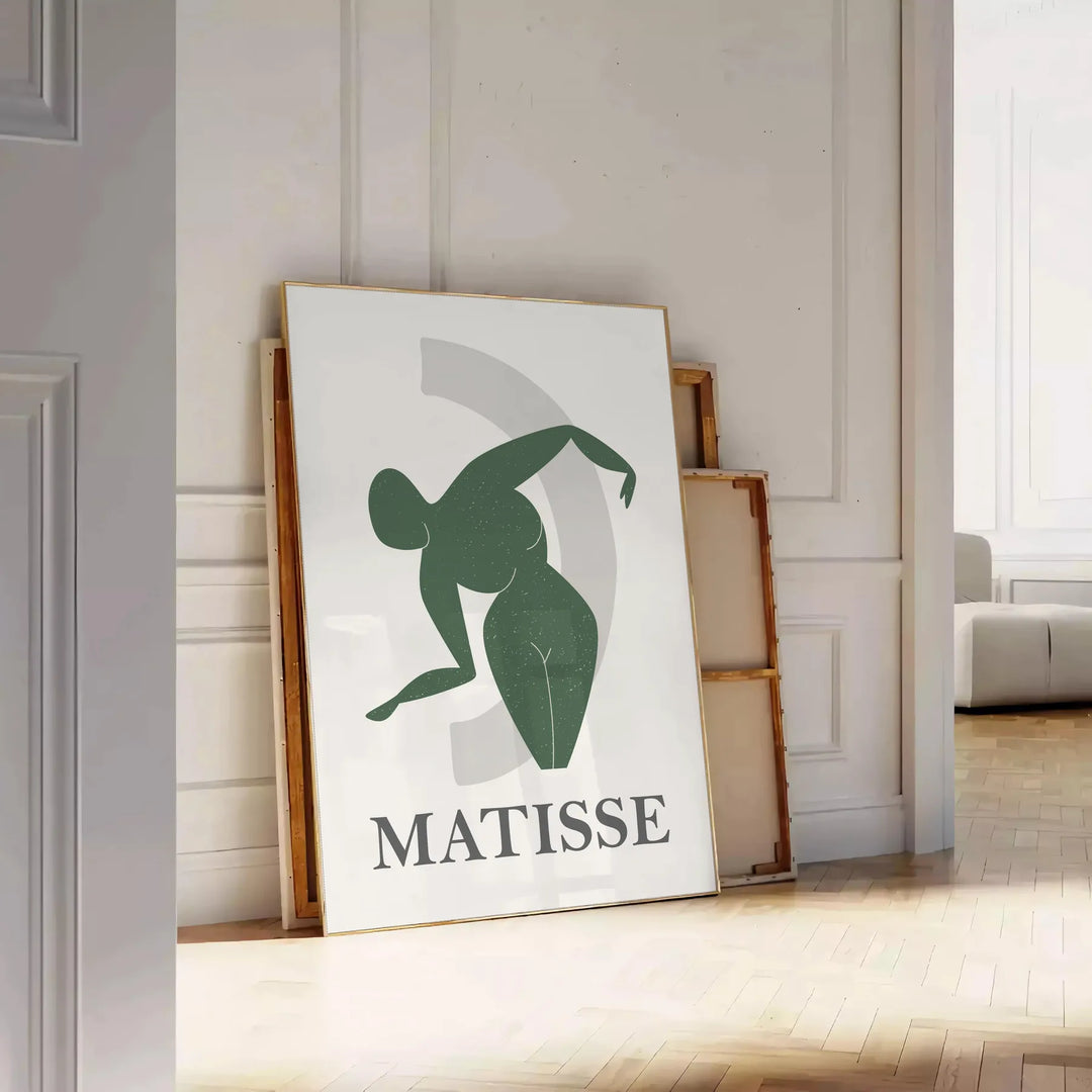 Plakāts bez rāmja ar krāsainu Matisse darbu grieztā papīra tehnikā, abstraktas formas - atbalstīts uz skujiņas grīdas pie baltas paneļu sienas