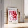 Poster showing Matisse-style papier découpé abstract red and gray shapes - leaning on a herringbone floor against a white panelled wall