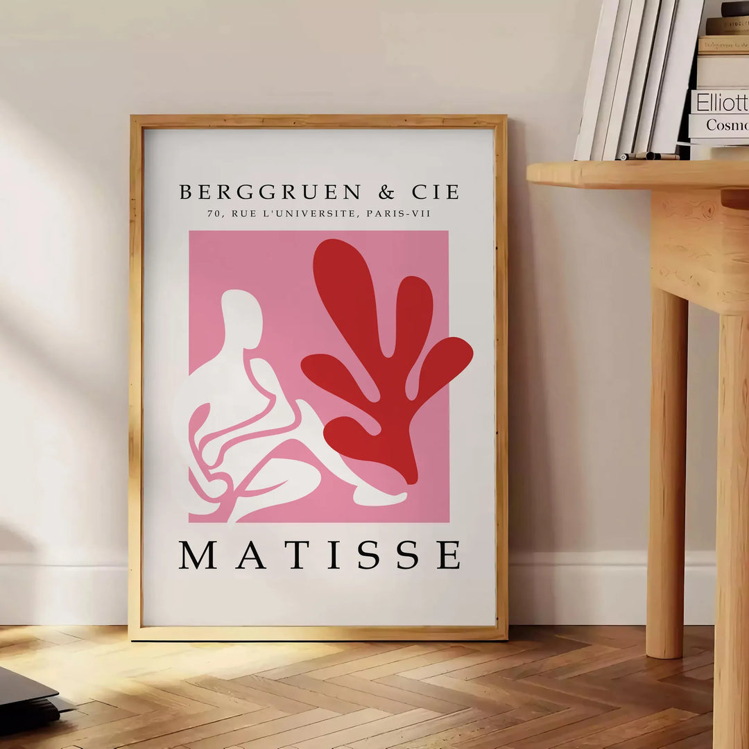 Poster showing Matisse-style papier découpé abstract red and gray shapes - beside a round wooden side table with books
