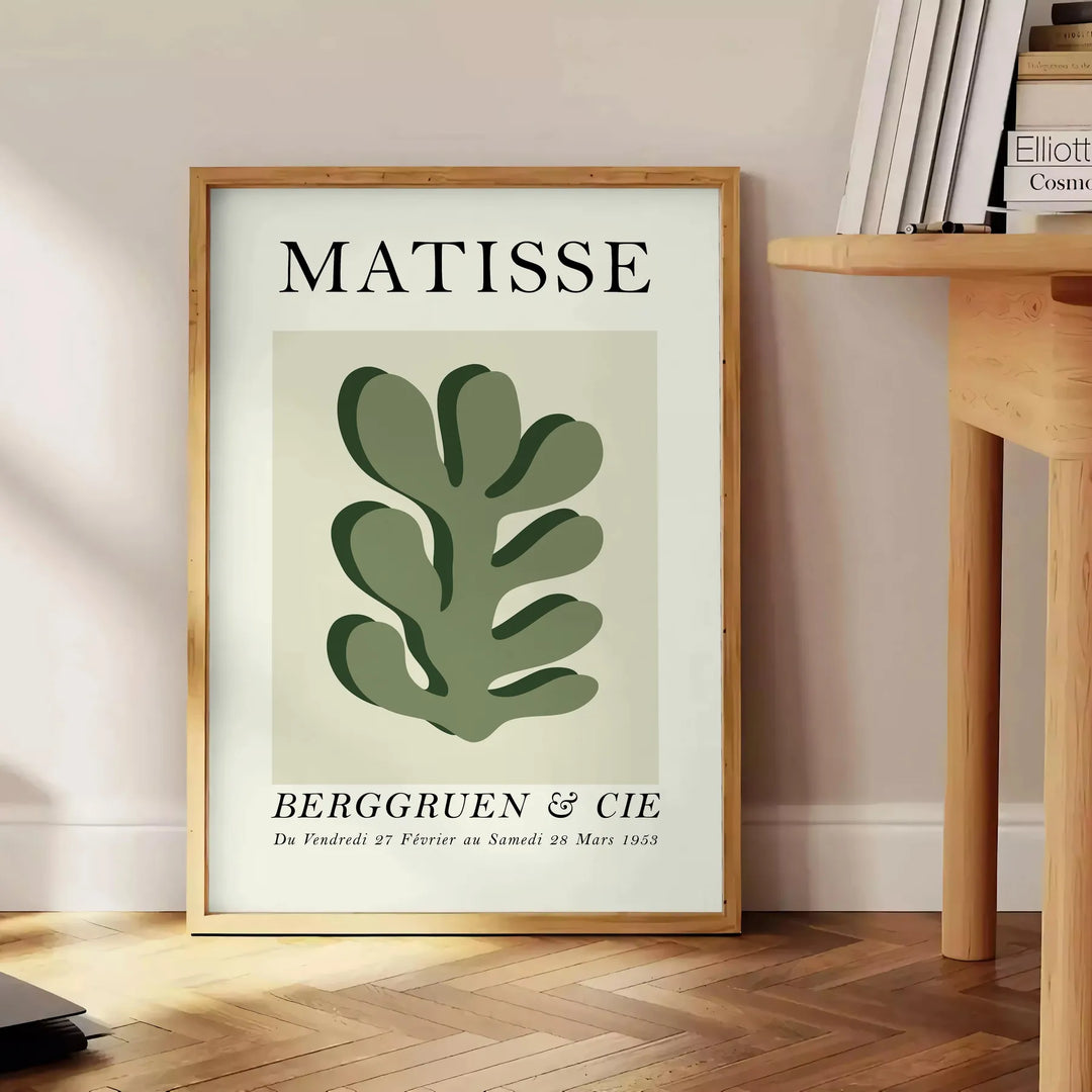 Matisse papier découpés poster with gray and white abstract cutout shapes - beside a round wooden side table with books