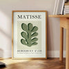Matisse papier découpés poster with gray and white abstract cutout shapes - beside a round wooden side table with books