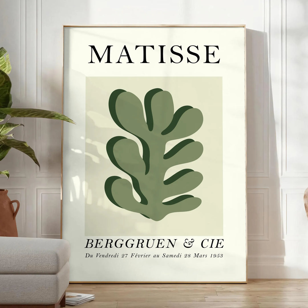 Matisse papier découpés poster with gray and white abstract cutout shapes - in a bright minimalist room with a plant and an armchair
