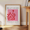 Abstract cut-paper collage by Matisse featuring gray and red shapes - beside a round wooden side table with books