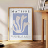 Poster showing Matisse paper cut-out artwork in bold abstract shapes - beside a round wooden side table with books