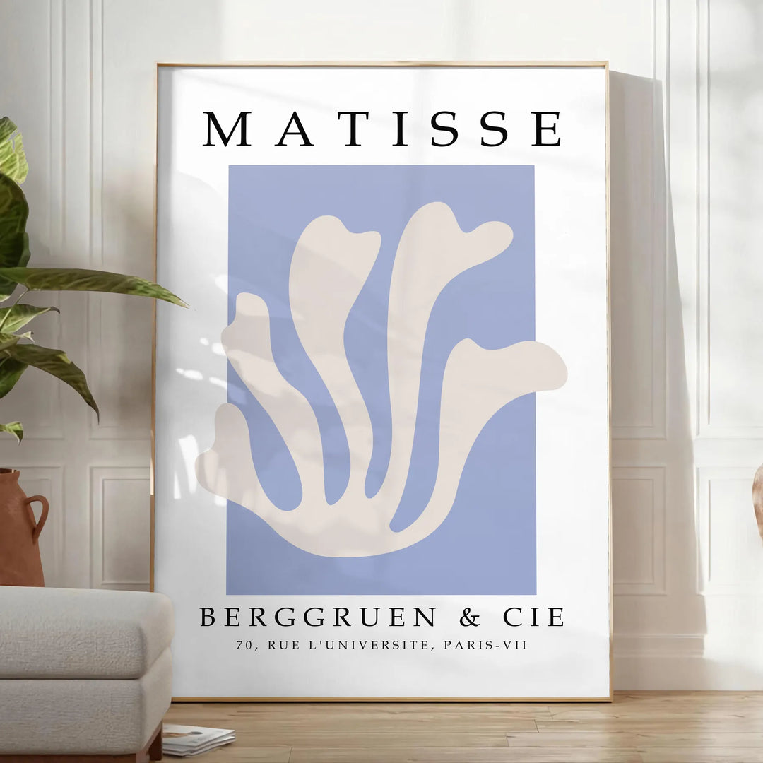 Poster showing Matisse paper cut-out artwork in bold abstract shapes - in a bright minimalist room with a plant and an armchair